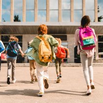 Little kids schoolchildren pupils students running hurrying to the school building for classes lessons from to the school bus. Welcome back to school. The new academic semester year start