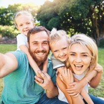 Nature, selfie and portrait of a happy family on a picnic together in outdoor green garden. Happy, smile and parents playing, hugging and bonding with children outside in backyard or park in canada